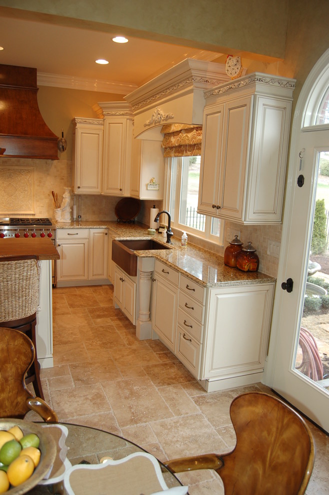 This is an example of a mid-sized traditional l-shaped kitchen in Atlanta with a farmhouse sink, raised-panel cabinets, distressed cabinets, granite benchtops, beige splashback, subway tile splashback, stainless steel appliances, travertine floors and with island.