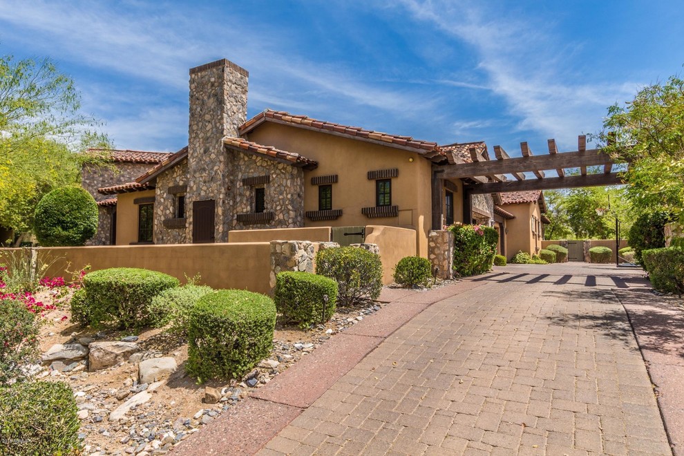 Photo of an expansive mediterranean one-storey multi-coloured house exterior in Phoenix with stone veneer, a gable roof and a tile roof.