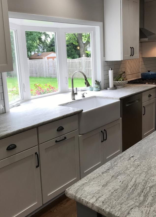Design ideas for a mid-sized country l-shaped open plan kitchen in Chicago with a farmhouse sink, shaker cabinets, white cabinets, granite benchtops, white splashback, subway tile splashback, stainless steel appliances, dark hardwood floors, with island and brown floor.