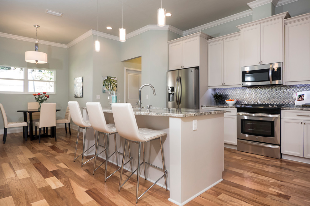 Contemporary kitchen in Jacksonville with a double-bowl sink, shaker cabinets, white cabinets, granite benchtops, metallic splashback, mirror splashback, stainless steel appliances, light hardwood floors and with island.