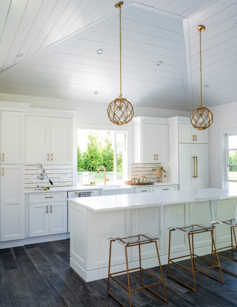 This is an example of a beach style single-wall open plan kitchen in New York with a farmhouse sink, shaker cabinets, white cabinets, quartz benchtops, multi-coloured splashback, panelled appliances, dark hardwood floors, with island, black floor, white benchtop, timber and vaulted.