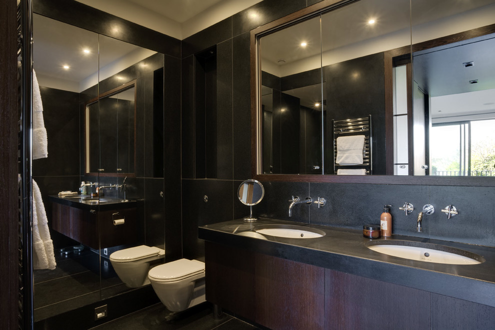 Inspiration for a mid-sized contemporary master bathroom in London with flat-panel cabinets, dark wood cabinets, black tile, an open shower, a wall-mount toilet, stone slab, black walls, marble floors, a drop-in sink, granite benchtops, black floor, a hinged shower door and black benchtops.