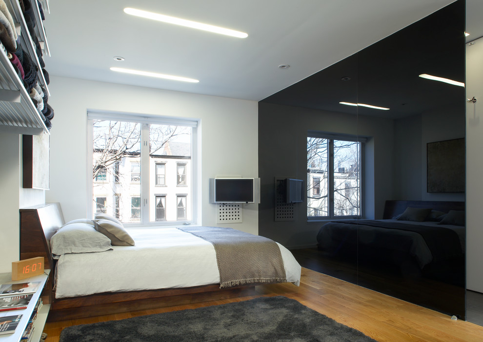 Photo of a mid-sized modern loft-style bedroom in New York with white walls, medium hardwood floors and green floor.
