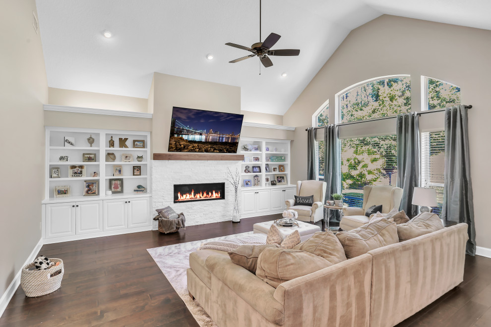 This is an example of a transitional open concept living room in Jacksonville with dark hardwood floors, a ribbon fireplace, a wall-mounted tv, brown floor and vaulted.