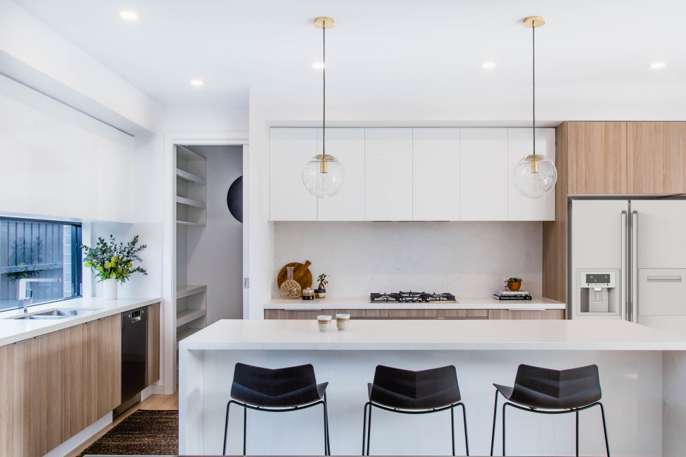 Inspiration for a large contemporary l-shaped open plan kitchen in Melbourne with a double-bowl sink, flat-panel cabinets, light wood cabinets, quartz benchtops, white splashback, stainless steel appliances, light hardwood floors, with island, brown floor and white benchtop.