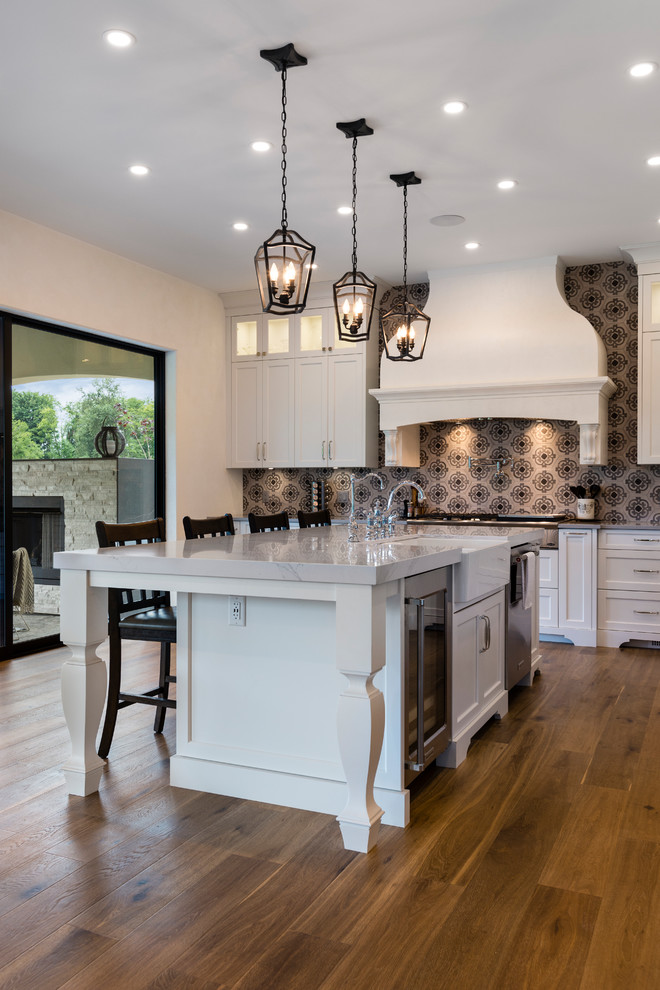 Photo of a large transitional open plan kitchen in Vancouver with a farmhouse sink, shaker cabinets, white cabinets, quartz benchtops, multi-coloured splashback, porcelain splashback, stainless steel appliances, medium hardwood floors, with island and brown floor.