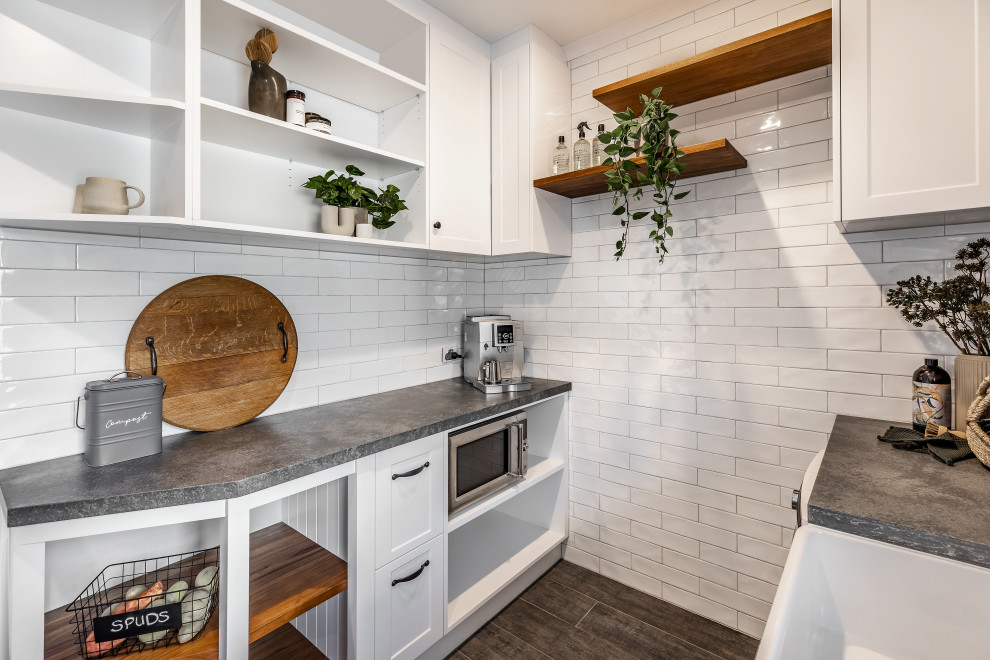 Lantlig inredning av ett stort grå grått kök, med en rustik diskho, skåp i shakerstil, vita skåp, bänkskiva i kvarts, vitt stänkskydd, stänkskydd i metallkakel, svarta vitvaror, klinkergolv i keramik, en halv köksö och grått golv