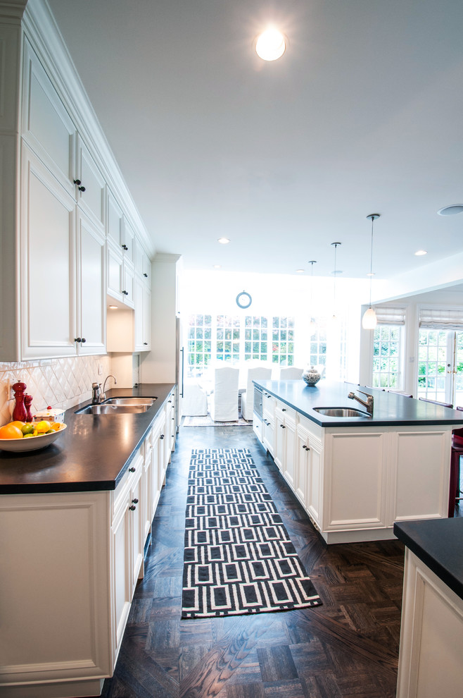 Large traditional l-shaped eat-in kitchen in Vancouver with a double-bowl sink, raised-panel cabinets, white cabinets, stainless steel appliances, dark hardwood floors, with island, white splashback and porcelain splashback.