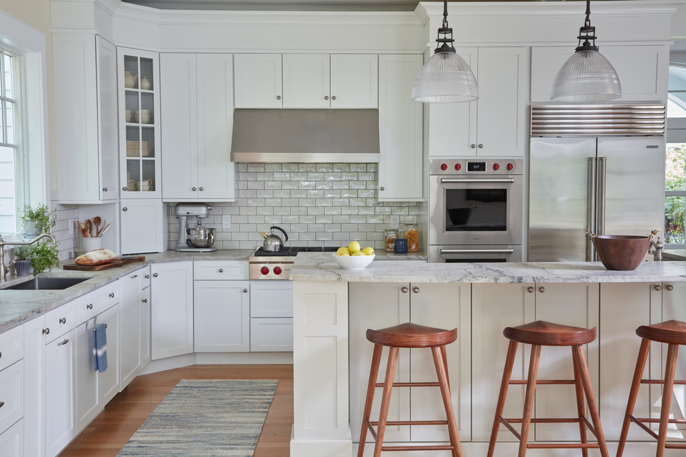 Design ideas for a mid-sized beach style l-shaped kitchen in DC Metro with a single-bowl sink, white cabinets, quartzite benchtops, white splashback, stainless steel appliances, with island, grey benchtop, shaker cabinets, subway tile splashback and light hardwood floors.