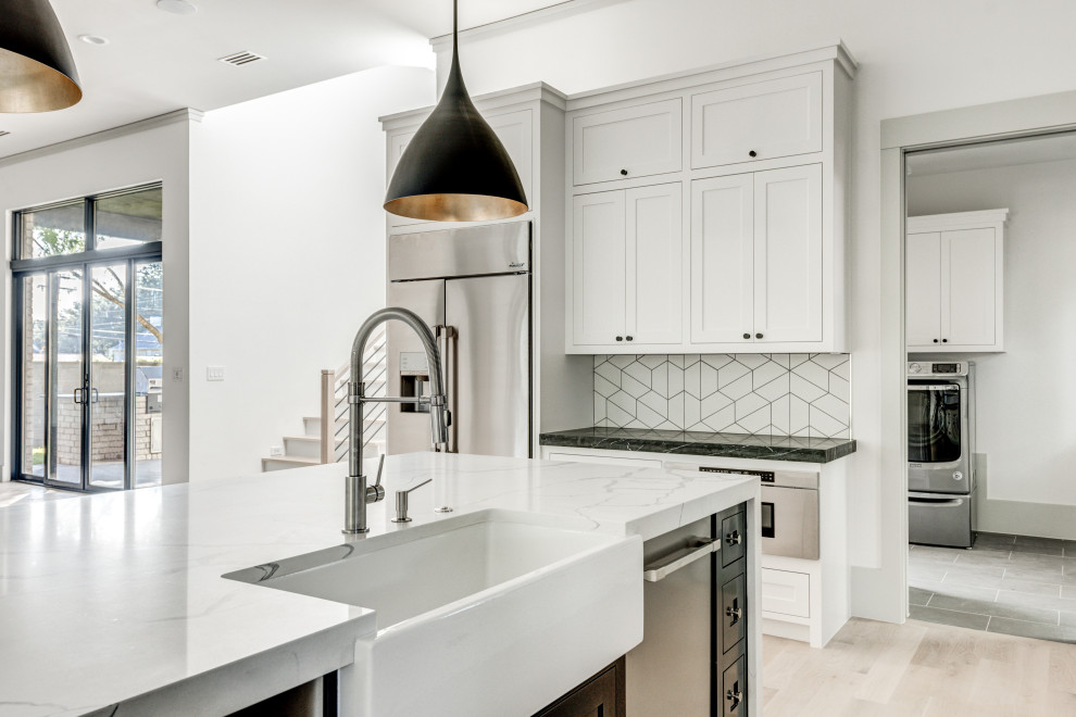 Open concept kitchen - transitional l-shaped light wood floor and white floor open concept kitchen idea in Dallas with a farmhouse sink, shaker cabinets, white cabinets, quartz countertops, white backsplash, ceramic backsplash, stainless steel appliances, an island and white countertops