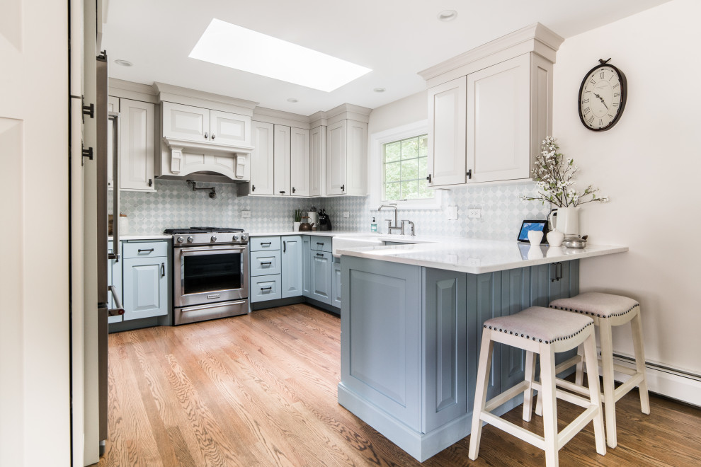 Inspiration for a transitional u-shaped separate kitchen in Chicago with a farmhouse sink, raised-panel cabinets, blue cabinets, multi-coloured splashback, stainless steel appliances, medium hardwood floors, a peninsula and brown floor.