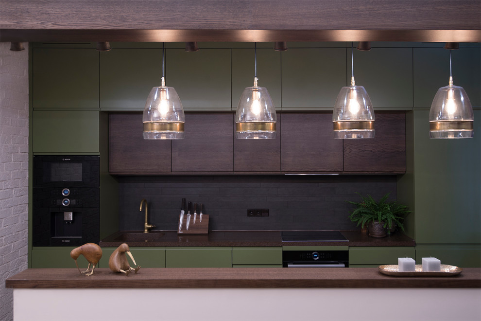 This is an example of a contemporary galley open plan kitchen in Moscow with a single-bowl sink, flat-panel cabinets, green cabinets, brown splashback and black appliances.