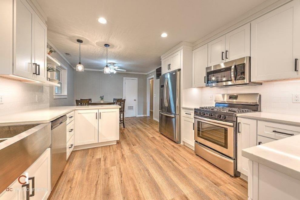 Eat-in kitchen - mid-sized modern l-shaped vinyl floor and multicolored floor eat-in kitchen idea with a double-bowl sink, shaker cabinets, white cabinets, quartz countertops, white backsplash, subway tile backsplash, stainless steel appliances, a peninsula and white countertops