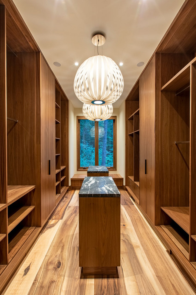 This is an example of a large contemporary gender-neutral walk-in wardrobe in Other with flat-panel cabinets, medium wood cabinets, medium hardwood floors and brown floor.