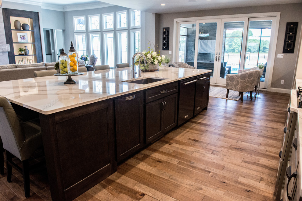 Open concept kitchen - huge transitional l-shaped medium tone wood floor and brown floor open concept kitchen idea with a single-bowl sink, glass-front cabinets, gray cabinets, quartz countertops, gray backsplash, ceramic backsplash, stainless steel appliances, an island and white countertops