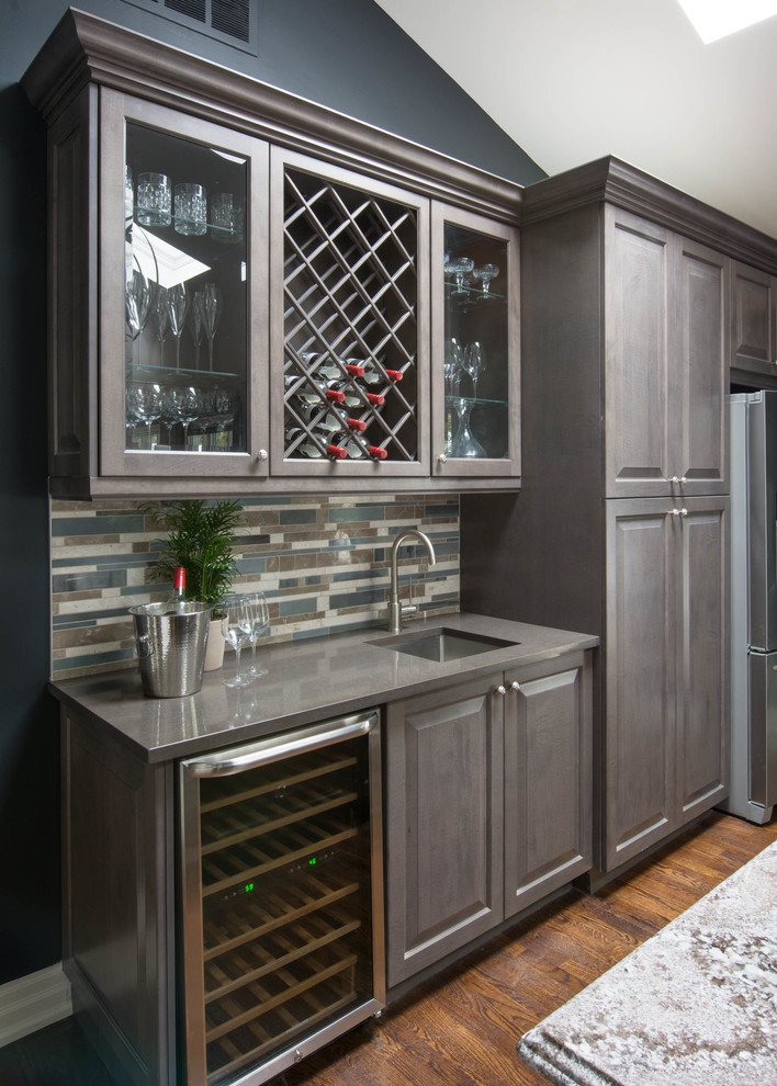 Small contemporary single-wall wet bar in Toronto with raised-panel cabinets, brown cabinets, quartzite benchtops, multi-coloured splashback, stone tile splashback, medium hardwood floors and an undermount sink.