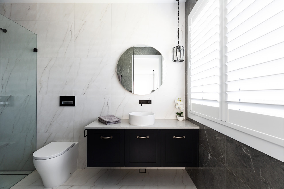 This is an example of a mid-sized beach style 3/4 bathroom in Sydney with recessed-panel cabinets, black cabinets, a curbless shower, a wall-mount toilet, white tile, ceramic tile, white walls, a drop-in sink, granite benchtops, a hinged shower door, white benchtops, a single vanity and a floating vanity.