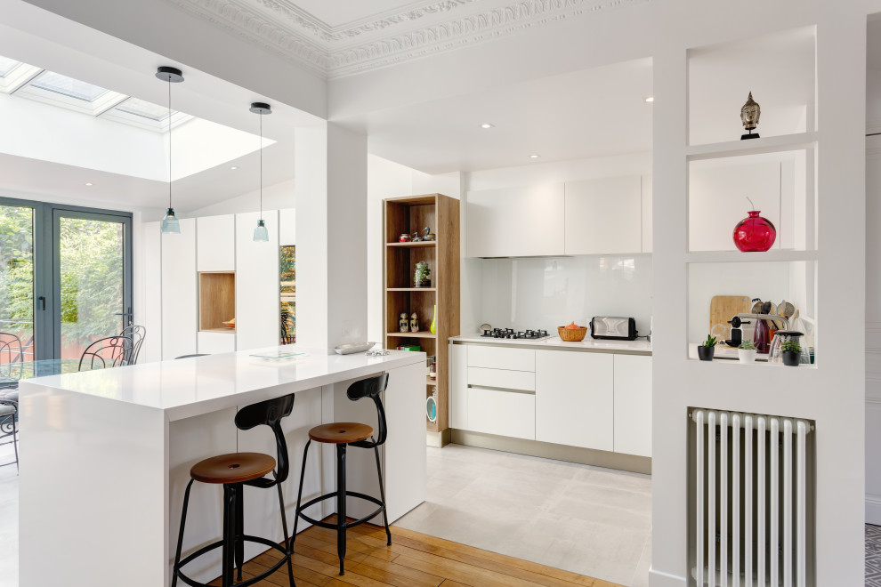 Large contemporary l-shaped open plan kitchen in Paris with a single-bowl sink, flat-panel cabinets, white cabinets, quartzite benchtops, white splashback, glass sheet splashback, panelled appliances, ceramic floors, with island, grey floor, white benchtop and recessed.