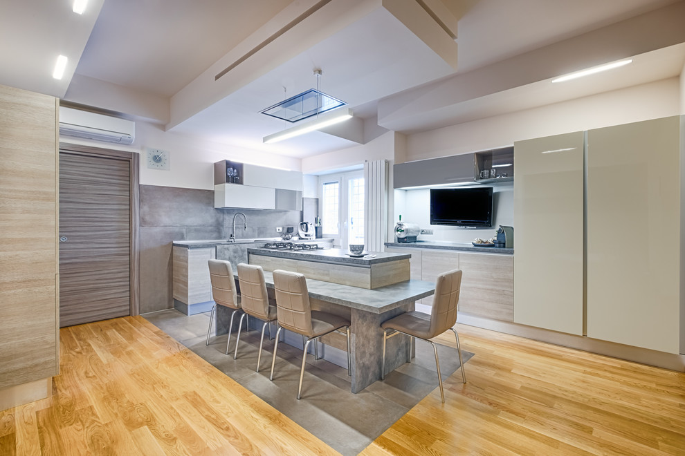 Large contemporary l-shaped open plan kitchen in Rome with flat-panel cabinets, with island, limestone benchtops, grey splashback, panelled appliances, medium hardwood floors, brown floor, light wood cabinets, cement tile splashback, grey benchtop and a drop-in sink.