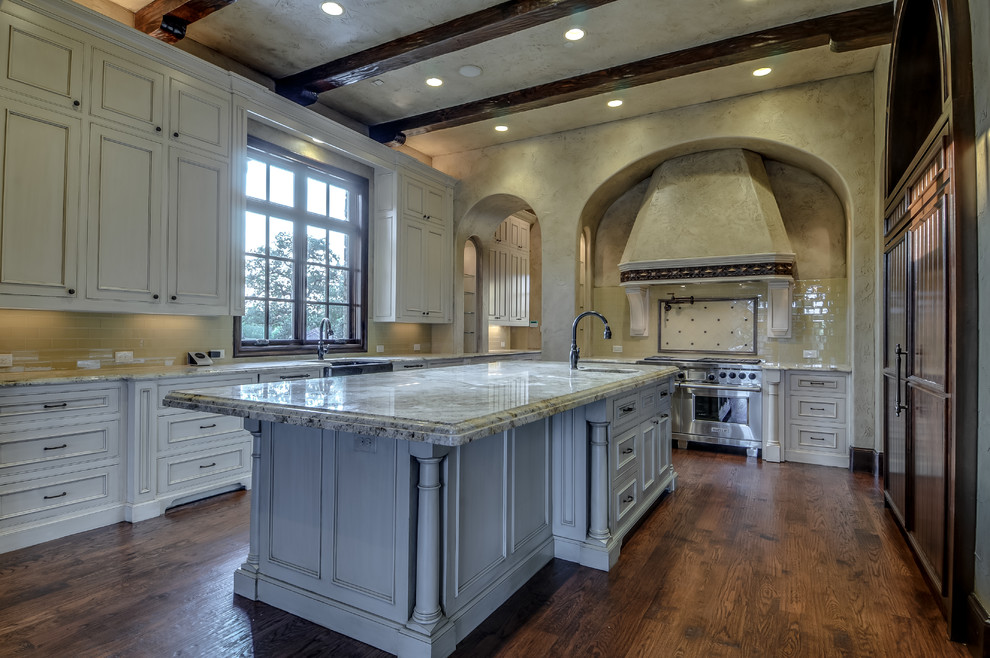 Inspiration for a large mediterranean separate kitchen in Dallas with a farmhouse sink, white cabinets, granite benchtops, beige splashback, stainless steel appliances, medium hardwood floors and with island.