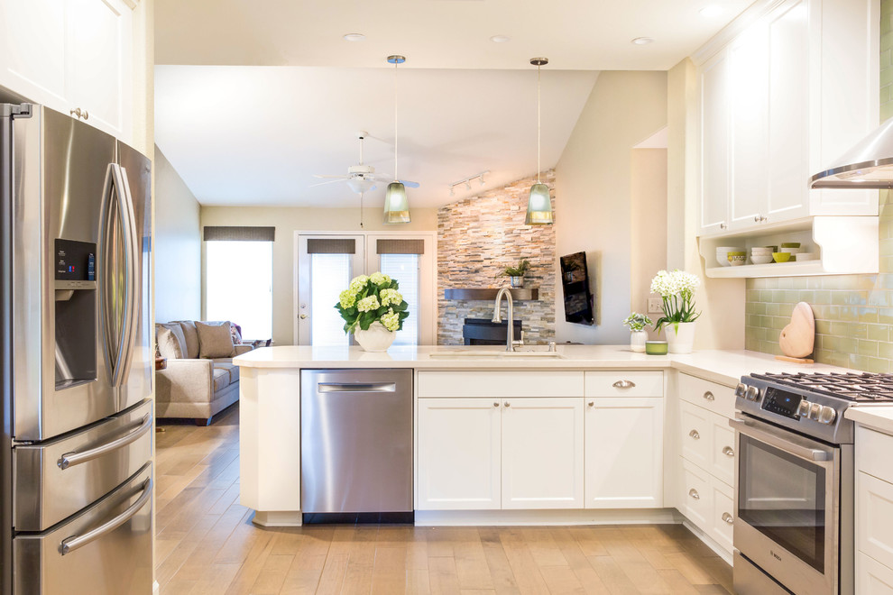 Example of a medium tone wood floor kitchen design with an undermount sink, recessed-panel cabinets, white cabinets, quartz countertops, green backsplash, subway tile backsplash, stainless steel appliances and a peninsula