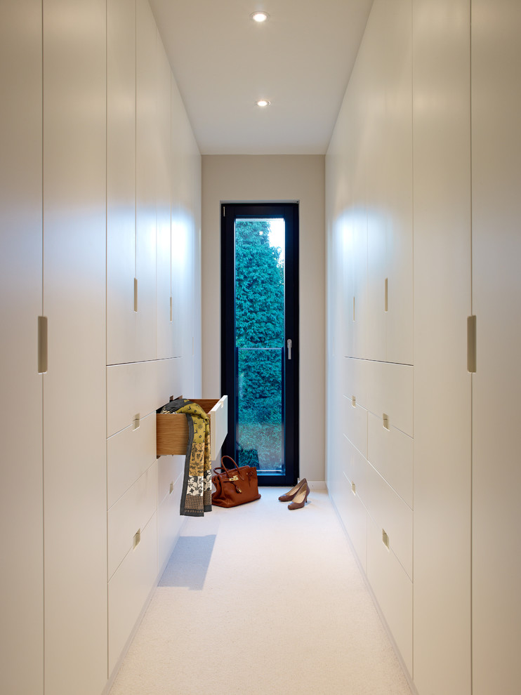 Design ideas for a large modern gender-neutral dressing room in Other with flat-panel cabinets, white cabinets and carpet.