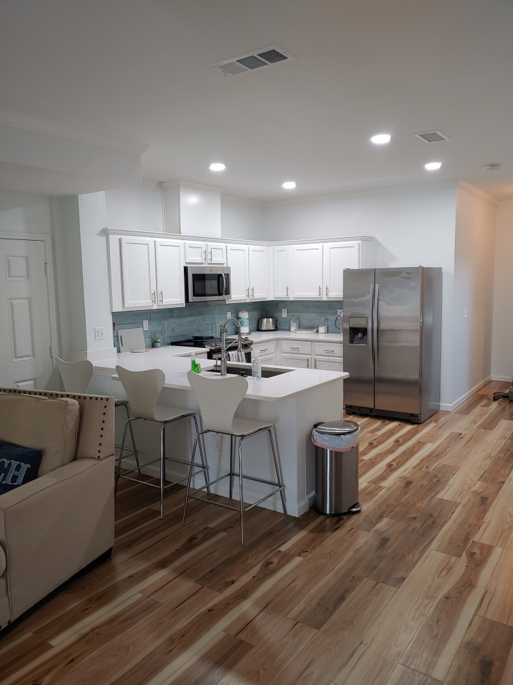 This is an example of a medium sized nautical u-shaped kitchen in Houston with a submerged sink, shaker cabinets, white cabinets, quartz worktops, blue splashback, porcelain splashback, stainless steel appliances, laminate floors, a breakfast bar, multi-coloured floors and white worktops.