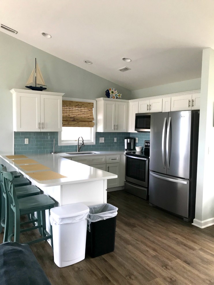 Photo of a mid-sized beach style u-shaped eat-in kitchen with an undermount sink, shaker cabinets, white cabinets, blue splashback, subway tile splashback, stainless steel appliances, dark hardwood floors, a peninsula, brown floor and blue benchtop.