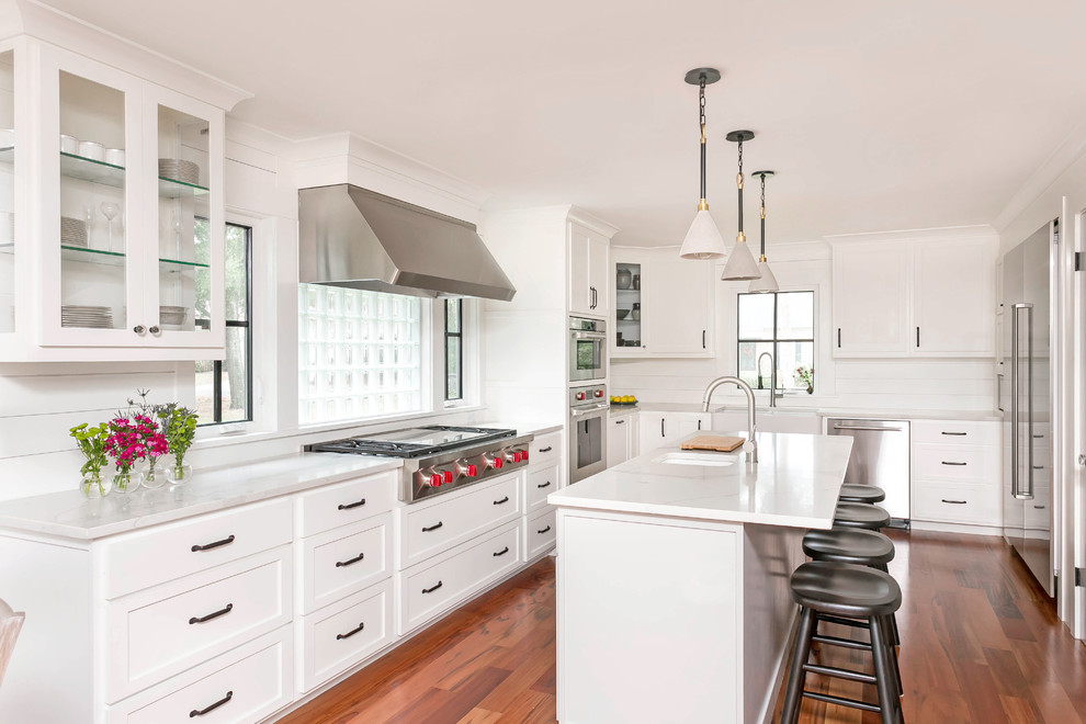 Inspiration for a transitional l-shaped medium tone wood floor and brown floor kitchen remodel in Charleston with a double-bowl sink, shaker cabinets, white cabinets, white backsplash, wood backsplash, stainless steel appliances, an island and white countertops