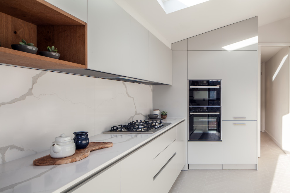 Design ideas for a mid-sized modern l-shaped kitchen in London with an undermount sink, flat-panel cabinets, quartzite benchtops, white splashback, engineered quartz splashback, no island, white benchtop, black appliances, white cabinets, grey floor and vaulted.
