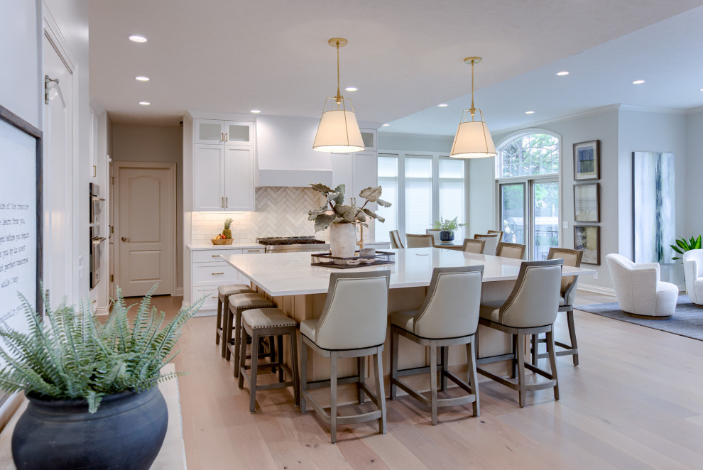 Example of a transitional light wood floor and beige floor open concept kitchen design with an undermount sink, white cabinets, quartzite countertops, multicolored backsplash, stainless steel appliances and an island