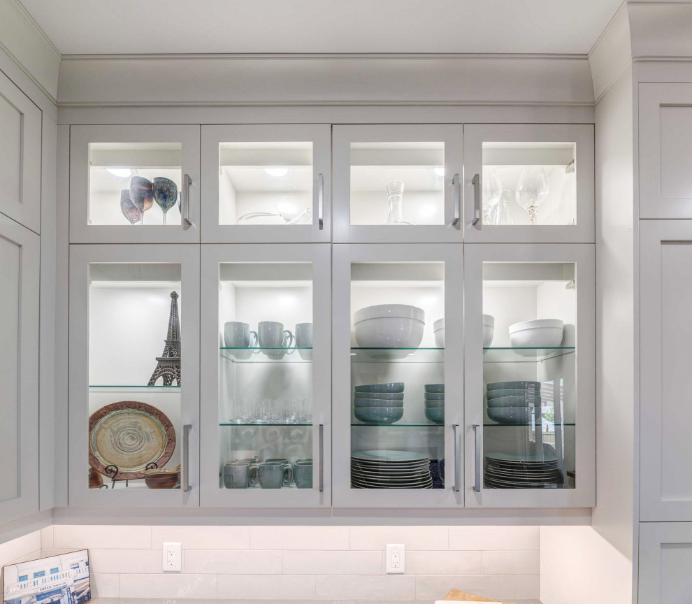 Inspiration for a transitional l-shaped kitchen remodel with a farmhouse sink, shaker cabinets, white cabinets, quartz countertops, porcelain backsplash, stainless steel appliances, an island and white countertops