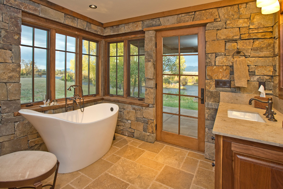 Mid-sized country master bathroom in Other with an undermount sink, furniture-like cabinets, dark wood cabinets, granite benchtops, a freestanding tub, multi-coloured tile, stone slab and travertine floors.