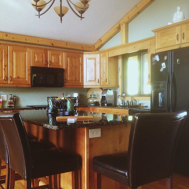 Photo of a mid-sized country l-shaped open plan kitchen in Other with an undermount sink, raised-panel cabinets, medium wood cabinets, granite benchtops, black appliances, medium hardwood floors and with island.