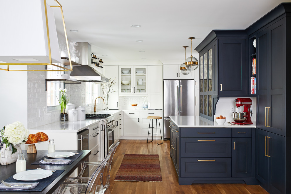 Design ideas for a mid-sized transitional l-shaped eat-in kitchen with shaker cabinets, blue cabinets, white splashback, subway tile splashback, medium hardwood floors, brown floor, quartz benchtops, stainless steel appliances, a peninsula, white benchtop and a single-bowl sink.