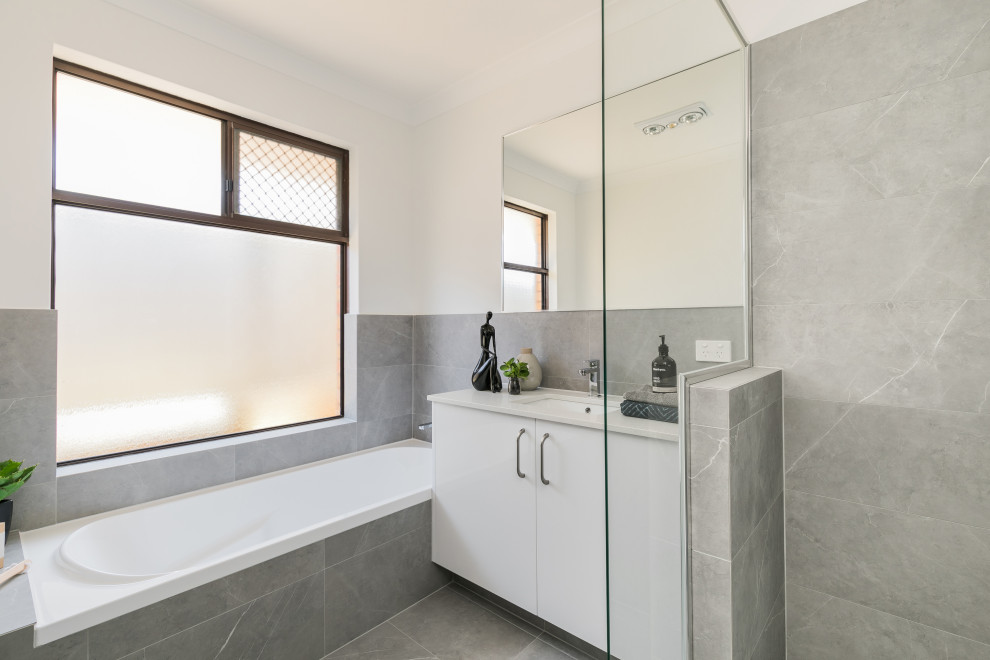 Design ideas for a mid-sized contemporary master bathroom in Perth with flat-panel cabinets, white cabinets, a drop-in tub, gray tile, white walls, an undermount sink, grey floor and beige benchtops.