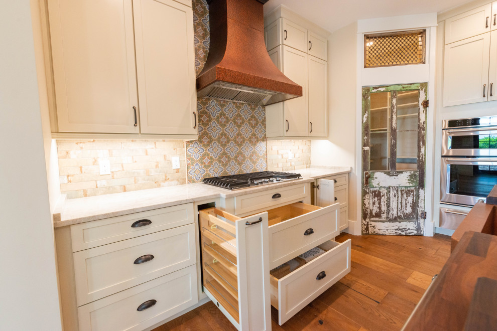 Mid-sized country kitchen pantry in Miami with a farmhouse sink, shaker cabinets, white cabinets, wood benchtops, multi-coloured splashback, porcelain splashback, stainless steel appliances, medium hardwood floors, with island, brown floor and brown benchtop.