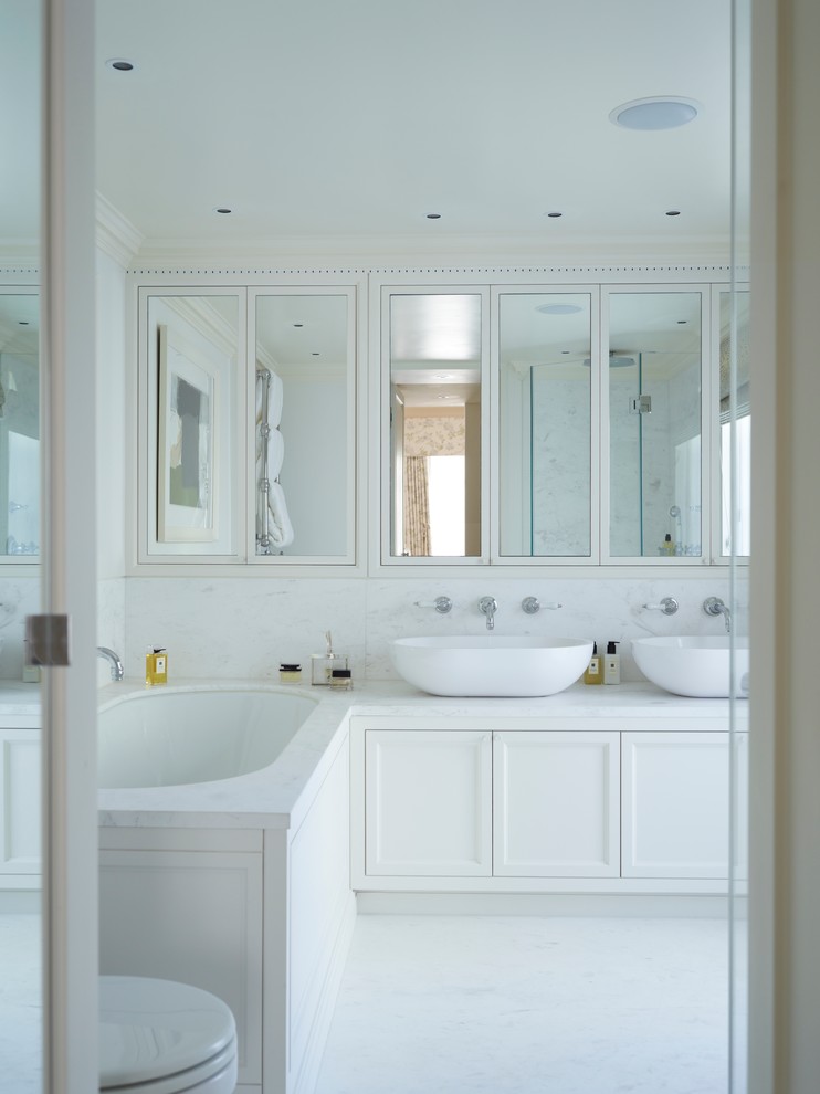 This is an example of a transitional master bathroom in London with a vessel sink, white cabinets, an undermount tub, white tile, white walls, recessed-panel cabinets and white benchtops.