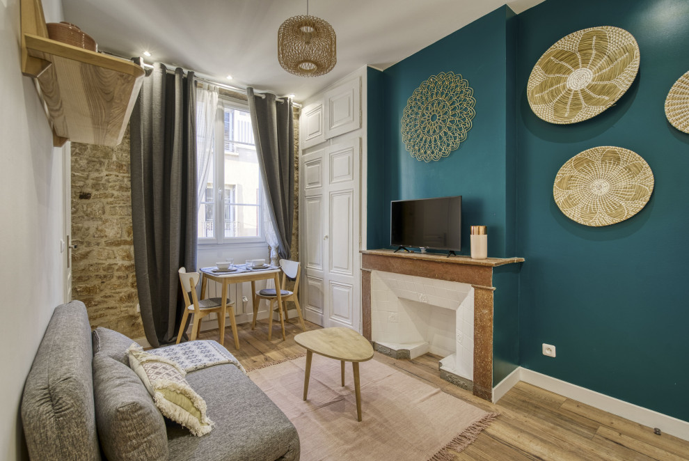 Kleines, Offenes Skandinavisches Wohnzimmer mit grüner Wandfarbe, braunem Holzboden, Kamin, Kaminumrandung aus gestapelten Steinen und freistehendem TV in Lyon