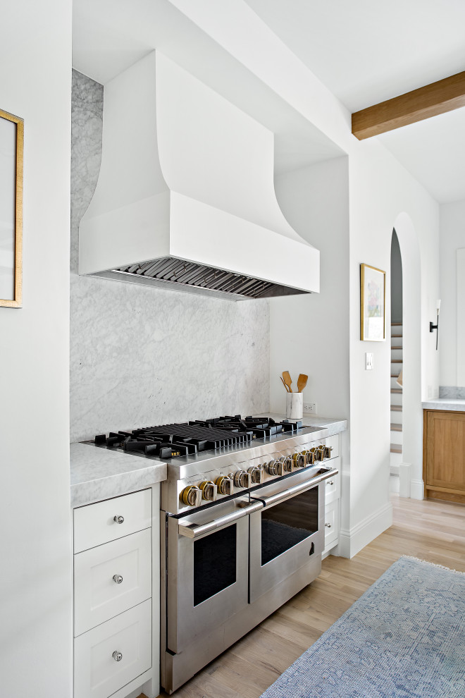 Inspiration for a large transitional l-shaped open plan kitchen in Dallas with an undermount sink, shaker cabinets, white cabinets, marble benchtops, white splashback, marble splashback, panelled appliances, light hardwood floors, with island, brown floor, white benchtop and exposed beam.