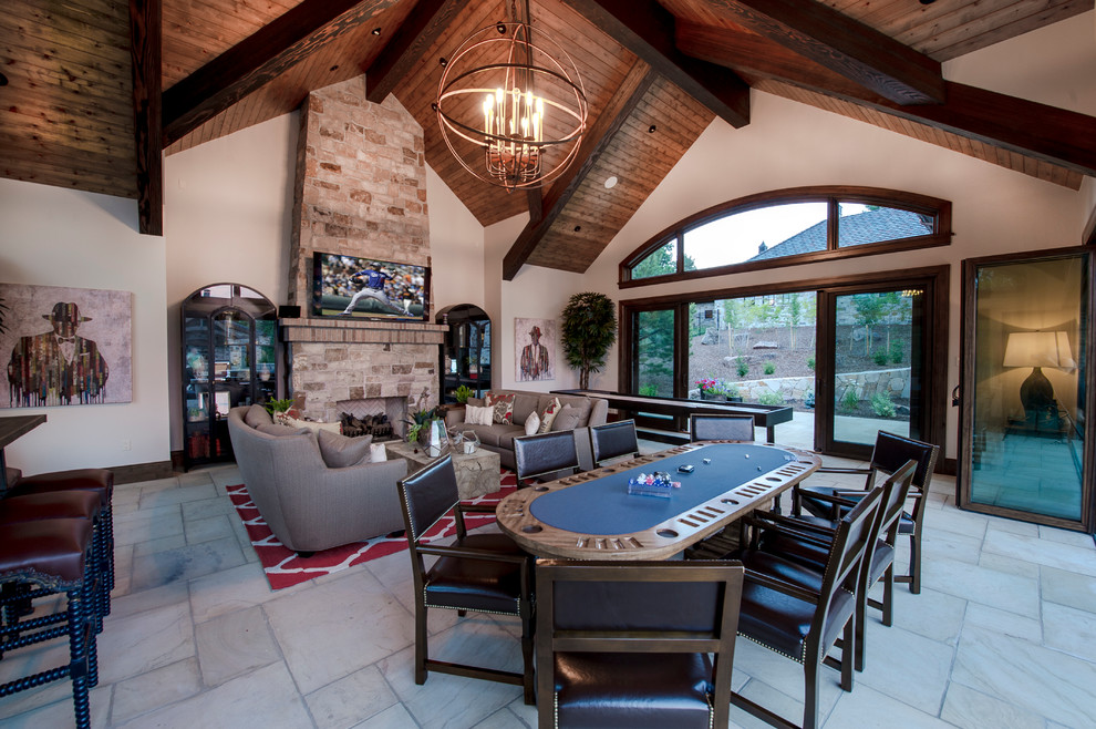 This is an example of an expansive country enclosed family room in Denver with a game room, a wall-mounted tv, beige walls, limestone floors, a standard fireplace, a stone fireplace surround and white floor.