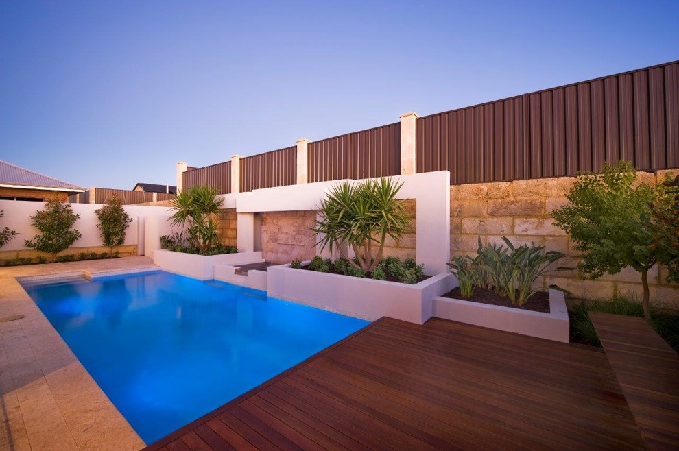 This is an example of a modern backyard rectangular lap pool in Perth with a water feature and natural stone pavers.