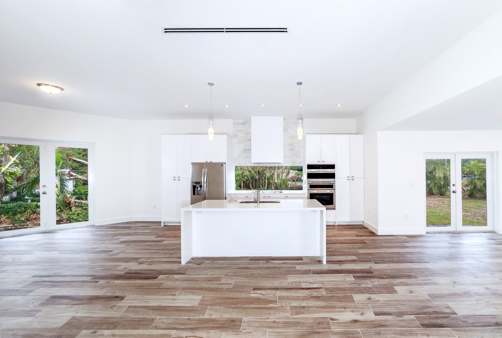 Inspiration for a mid-sized modern single-wall open plan kitchen in Miami with an undermount sink, shaker cabinets, white cabinets, marble benchtops, window splashback, stainless steel appliances, medium hardwood floors, with island, brown floor and white benchtop.