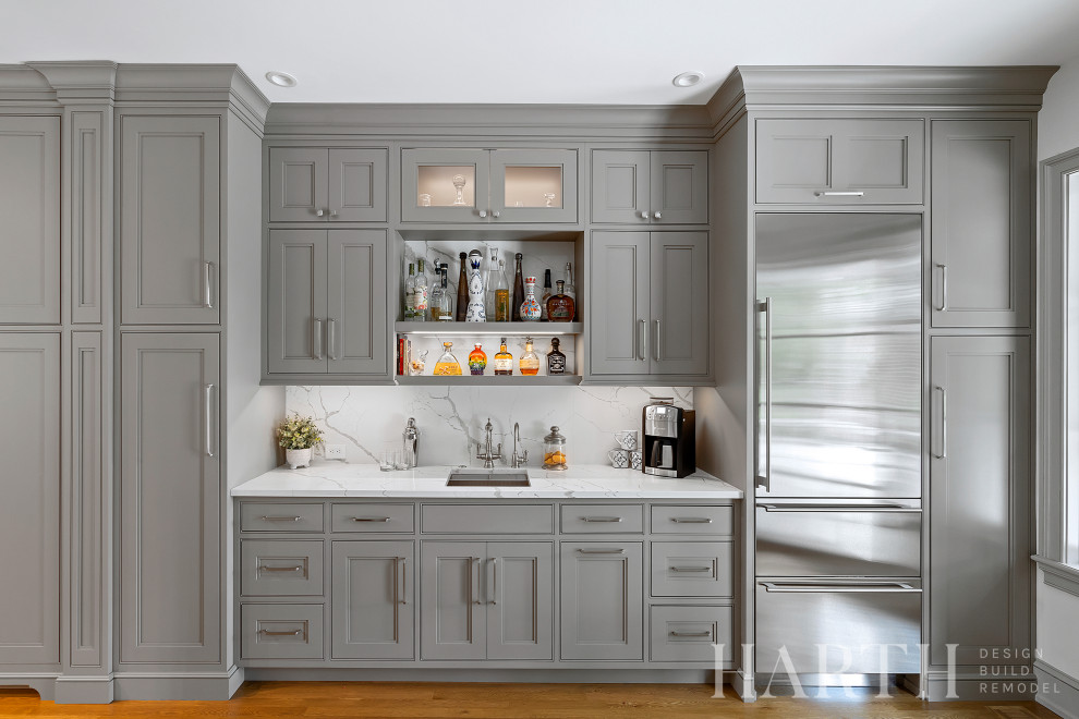 Mid-sized single-wall light wood floor and brown floor wet bar photo in Philadelphia with an undermount sink, beaded inset cabinets, gray cabinets, quartz countertops, white backsplash, quartz backsplash and white countertops