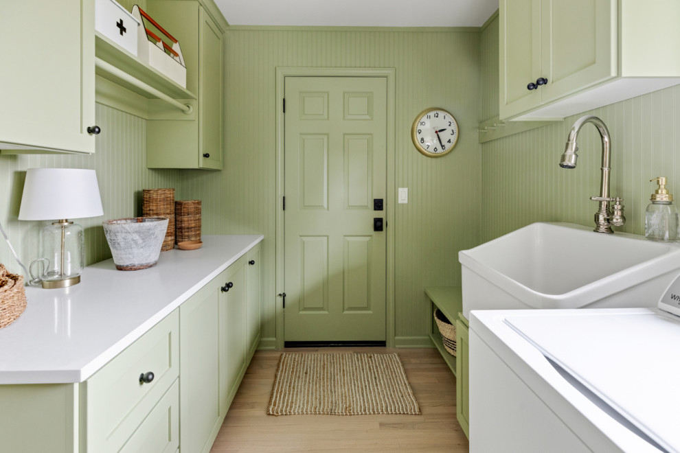 Expansive country galley dedicated laundry room in Other with a farmhouse sink, shaker cabinets, green cabinets, quartzite benchtops, green walls, light hardwood floors, a side-by-side washer and dryer and white benchtop.