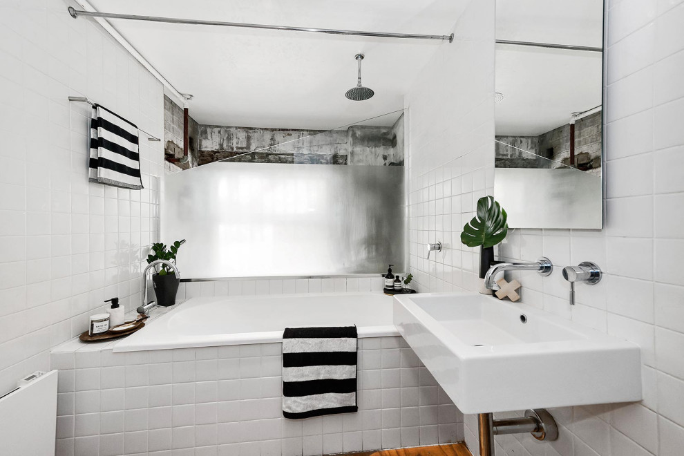 Diseño de cuarto de baño único urbano con bañera empotrada, combinación de ducha y bañera, baldosas y/o azulejos blancos, suelo de madera en tonos medios, lavabo suspendido, suelo marrón y ducha con cortina