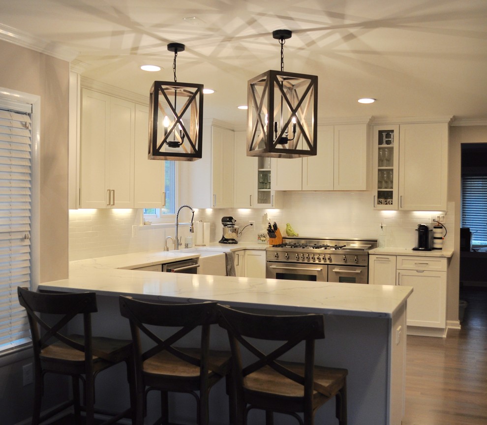 Mid-sized transitional u-shaped dark wood floor and brown floor kitchen photo in DC Metro with a farmhouse sink, shaker cabinets, white cabinets, marble countertops, white backsplash, subway tile backsplash, stainless steel appliances and a peninsula