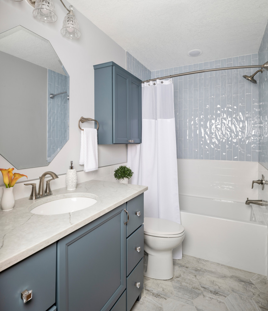 Design ideas for a small transitional master bathroom in Minneapolis with shaker cabinets, blue cabinets, an alcove tub, a shower/bathtub combo, a two-piece toilet, white tile, ceramic tile, grey walls, porcelain floors, an undermount sink, engineered quartz benchtops, grey floor, a shower curtain and white benchtops.