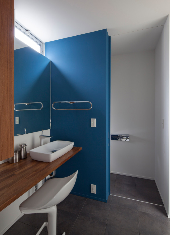 Aménagement d'un petit WC et toilettes moderne en bois foncé avec un placard sans porte, WC à poser, un mur bleu, un sol en carrelage de porcelaine, un plan de toilette en bois, un sol gris, un plan de toilette marron et meuble-lavabo encastré.