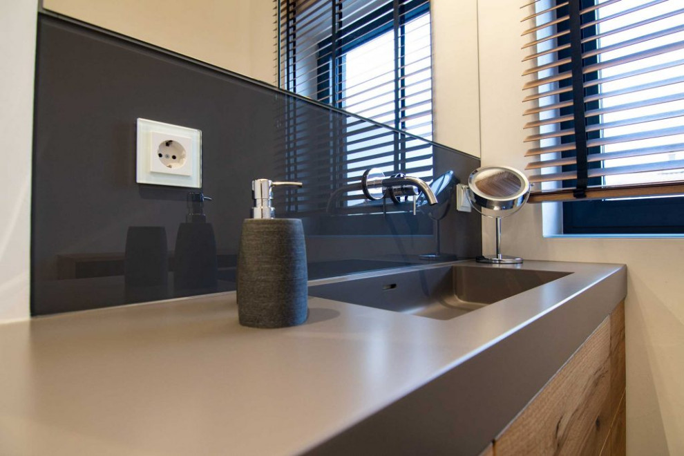 This is an example of a mid-sized contemporary master bathroom in Other with beaded inset cabinets, brown cabinets, a wall-mount toilet, white walls, an integrated sink, solid surface benchtops, black floor, grey benchtops, a single vanity and a floating vanity.